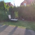 Garden with lounge chair, lawn, and hedges. Background: houses with roofs.