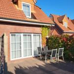 Terrace with table and chairs in front of a house with red roof and climbing plants.