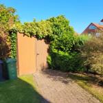 Paved path leads to a wooden door. Surrounded by green areas and shrubs.
