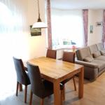 Dining room with wooden table and chairs, living area with sofa and windows