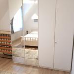 Bedroom with mirrored wardrobe, bed, and wooden floor.