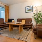 Wohnzimmer mit braunen Ledermöbeln, Holztisch und großem Fenster.