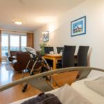 Wohn- und Essbereich mit Blick auf den See, Esstisch mit Stühlen und Bett im Vordergrund.