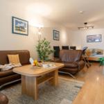 Wohnbereich mit braunen Ledersofas, Holztisch und Pflanzen. Im Hintergrund steht ein Bett.