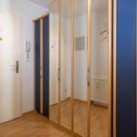 Flur mit Spiegeltüren und Holzboden. Tür mit Aufkleber und Intercom.