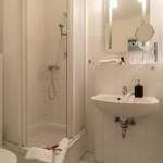 Badezimmer mit Dusche, Waschbecken und Toilette. Weiße Fliesen und Spiegel.