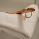 Ein weißes Handtuch liegt gefaltet auf einer Fläche, darauf ein hölzerner Körbchenhalter mit Seil.