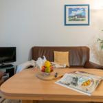 Ein Wohnzimmer mit braunem Sofa, Holztisch und Fernseher. Auf dem Tisch steht eine Obstschale.