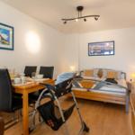 Schlafzimmer mit Bett, Esstisch und Stühlen. Wandbilder und Pflanze sind sichtbar.