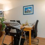 Essbereich mit Tisch, Stühlen und Hochstuhl. Wandbilder und Pflanze sind sichtbar.