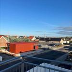 View from balcony over a street with a red container and houses under blue sky.