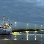 Fishing boat HM84 rests on the beach at night. Waves break against the pier.