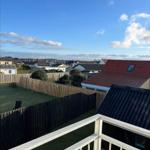Balcony view over rooftops and green lawn with wooden fences under blue sky.