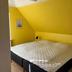 Bedroom with yellow walls, bed with patterned coverlet, and ceiling beams.