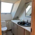 Bathroom with sloped ceiling, sink, mirror, and toilet. Window with view outside.