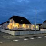 House with white facade, dark roof, and white fence. Windows are lit.