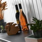 Two wine bottles, a wooden figure, and plants are on the work surface.