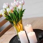 On the table, there are tulips in a glass and three lit candles on a tray.