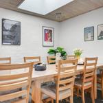 Dining room with wooden table, chairs, and wall art. Ceiling with skylight.