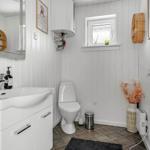 Bathroom with sink, toilet, and window. White walls, brown floor, and decorative items.