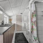 Bathroom with sink, shower, and toilet. Tile floor and wooden cabinets.