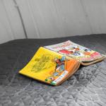 Two comic books rest on a bed with a dark, quilted bedspread.