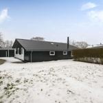 Black house with snow-covered grounds and hedges in winter.