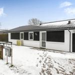 A white house with a black roof and shutters stands in the snow.