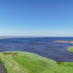 Wide view of coastal landscape with water, green areas, and holiday homes.