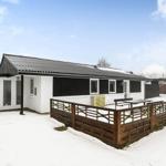 Modern villa with black-and-white design and snow-covered garden area with wooden railing.