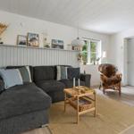 Ein Wohnzimmer mit grauem Sofa, Holztisch und Sessel. An der Wand hängen Bilder und Dekorationsgegenstände.