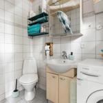 Badezimmer mit Toilette, Waschbecken und Waschmaschine. Weiße Fliesen und blau-grüne Handtücher.