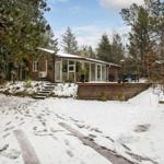 Holzhaus mit Glasfront und Terrasse im Schnee, umgeben von Bäumen.