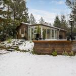Holzhaus mit Glasfront und Terrasse im Schnee, umgeben von Bäumen.