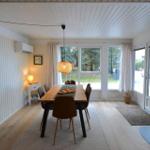 Esszimmer mit Holztisch, Stühlen und Fenstern zum Garten. Kamin und Deckenleuchte sichtbar.