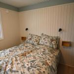 Schlafzimmer mit Bett, Fenster und Holzwandverkleidung. Zwei Nachttische und Wandlampen.