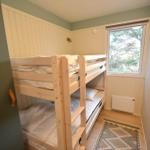 Zimmer mit Doppelstockbett, Fenster und Holzwandverkleidung.