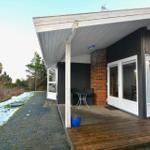 Haus mit Terrasse, Tisch und Stühlen. Schnee bedeckt den Boden. Holzterrasse und Fensterfront.