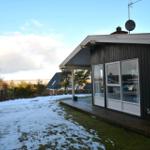 Ein dunkelholzverkleidetes Haus mit Glasfront und schneebedecktem Grundstück.