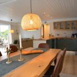 Essbereich mit Holztisch, Stühlen und Lampe. Küche mit grünen Schränken und Arbeitsplatte.