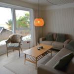 Wohnzimmer mit Sofa, Sessel und Tisch. Große Fenster mit Blick auf Außengelände.