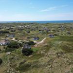 Dorf mit strohgedeckten Häusern auf grüner Dünenlandschaft, Blick auf das Meer.