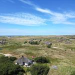 Dorf mit strohgedeckten Häusern auf Dünen, Blick auf Nordsee unter blauem Himmel.
