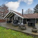 Haus mit Holzterrasse, Grill, Liegen und Tischen im Garten.