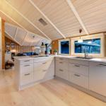 Küche mit Holzdecke, Fenstern und Arbeitsplatten. Wohnbereich im Hintergrund sichtbar.