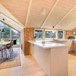 Küche mit Essbereich, Holzdecke und großen Fenstern. Weiße Arbeitsplatten und moderne Geräte.
