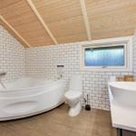 Badezimmer mit Badewanne, Toilette und Waschbecken unter Holzdecke mit weißen Fliesen.