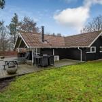 Schwarze Holzhütte mit Terrasse, Grill und Garten. Hintergrund: Wald und Himmel.