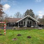 Haus mit Holzterrasse, Garten und Grillplatz. Umgeben von Bäumen und Grasfläche.