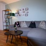 Ein Wohnzimmer mit grauem Sofa, zwei runden Tischen und einer Wand mit Bildern.